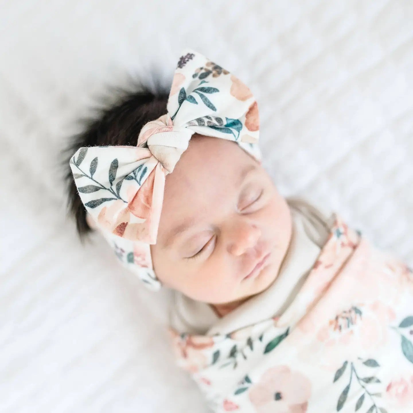 Newborn baby wearing a floral headband and swaddle on a soft surface