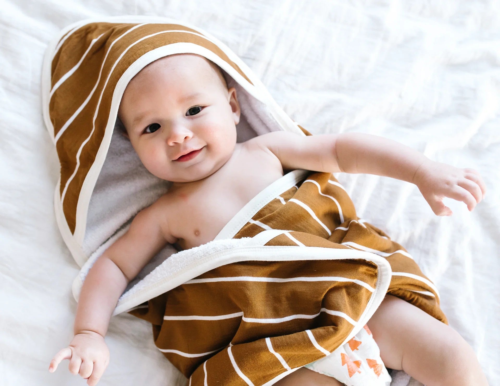 Baby wrapped in a brown and white striped towel on a white blanket