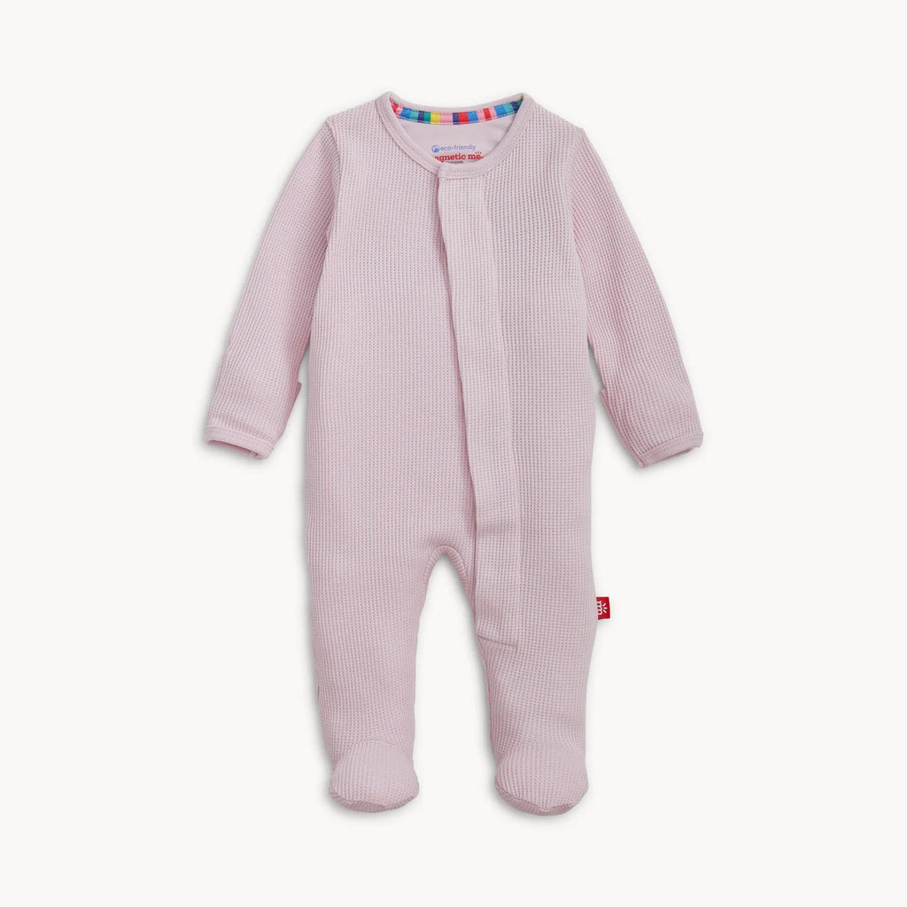 A baby footed sleeper in light pink waffle knit fabric, featuring a snap-button front closure and a small red tag near the lower leg, shown against a plain off-white background.