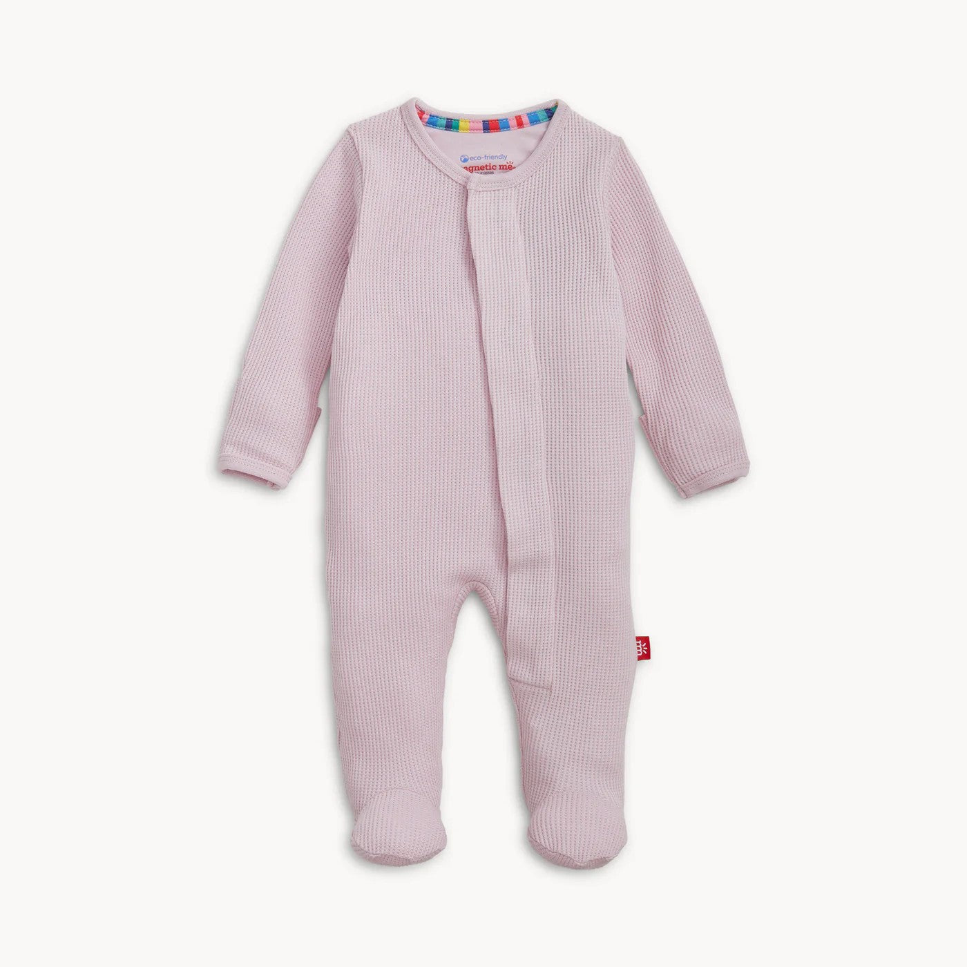 A baby footed sleeper in light pink waffle knit fabric, featuring a snap-button front closure and a small red tag near the lower leg, shown against a plain off-white background.