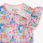A close-up of a children's short-sleeve top with a colorful floral print on a light blue background, featuring pink ruffled sleeves and a pink collar. The inner neck label shows the brand 'magnetic me'.