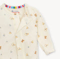 A close-up of a baby long-sleeve romper in cream-colored cotton fabric, featuring a playful print of teddy bears, bows, and arrows in brown, blue, and yellow. The brand 'Commette' is visible on the inner neck label along with 'eco-friendly' and 'cotton' text.