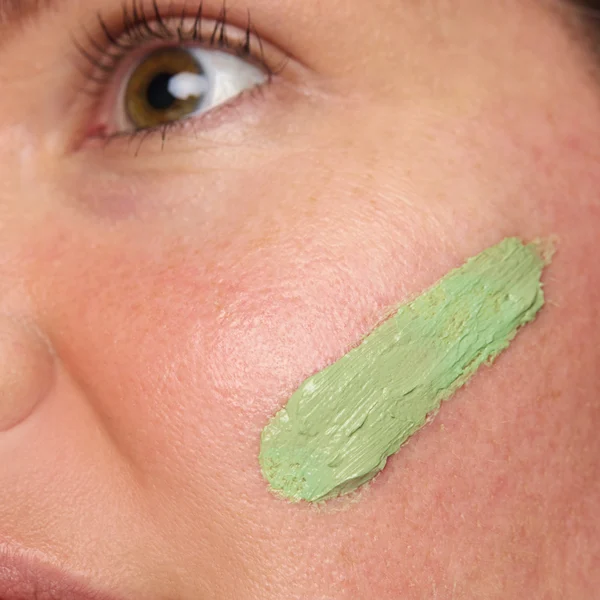 Close-up of a woman's cheek with a green color-correcting primer applied, demonstrating the smoothing effect of Red Correct Treatment Primer.