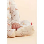 A close-up of a baby wearing a cream-colored footed sleeper with Winnie the Pooh print, resting on a matching cream pillow with a bear outline.