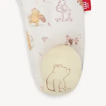 A close-up of a white baby sock featuring Winnie the Pooh illustrations in brown, with a cream-colored foot protector insert.