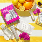 Clean Canvas Skincare Kit (Limited-Edition) displayed on a yellow and white striped towel with skincare products, a dish of citrus fruits, and vibrant pink flowers, evoking fresh and natural self-care.