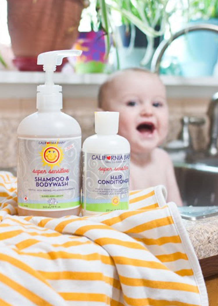 California Baby - (No Fragrance) Super Sensitive™ Hair Conditioner bottle next to matching shampoo and bodywash, with a joyful baby and cozy striped towel in a bright, natural setting.