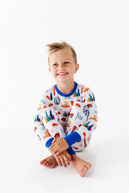 Smiling young boy sitting cross-legged wearing Two-Piece Pajamas - Bamboo - Blue Chicago featuring colorful Chicago-themed prints with blue cuffs, styled for cozy comfort and practical mom essentials.