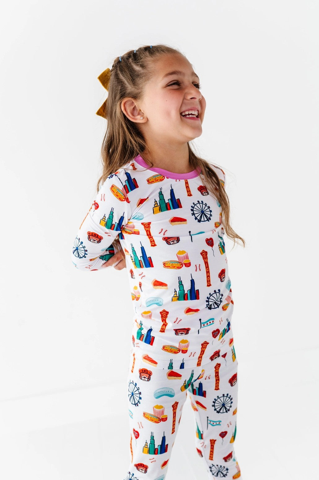 Smiling young girl wearing colorful Two-Piece Pajamas - Bamboo - Pink Chicago featuring playful Chicago-themed illustrations in soft bamboo fabric, perfect for cozy nights.