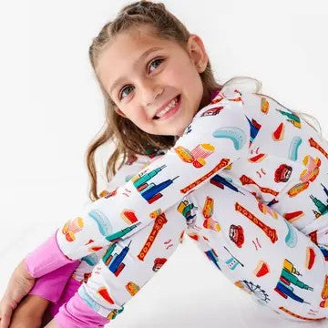 Smiling child wearing Two-Piece Pajamas - Bamboo - Pink Chicago with colorful Chicago-themed prints and soft pink cuffs, showcasing cozy and stylish kids clothing from a curated children’s boutique.