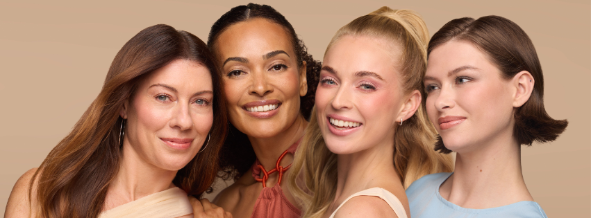 Four diverse women smiling closely together against a warm beige background, showcasing natural beauty and a sense of community in soft, neutral tones.
