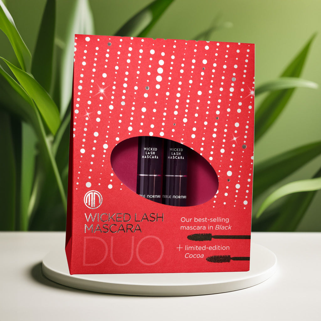 Merle Norman Cosmetics - Wicked Lash Mascara Duo (Limited-Edition) in festive red packaging featuring best-selling black and limited-edition cocoa mascaras, styled with natural greenery.
