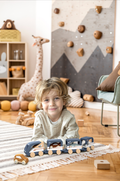 Young child playing with the Speedy Monkey - Train Vehicle Carrier wooden toy set on a cozy rug in a stylish children’s boutique room with soft, neutral decor and educational toys.