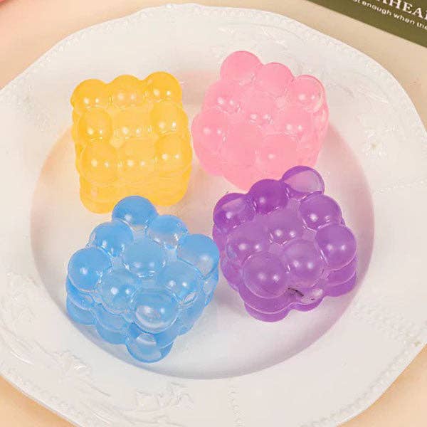 Four translucent bubble-shaped gel packs in yellow, pink, blue, and purple, arranged on a white plate.