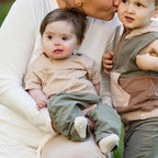 Mother holding and kissing two young children outdoors wearing soft neutral-colored clothing, featuring the Burt's Bees Baby - Drop Shoulder Infant Boy Tee Set in a cozy, stylish kids clothing setting.