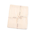 Folded cream-colored baby blanket tied with a branded ribbon, showcasing Viverano Organics - Milan Pastel Baby Blanket Sweater Knit (Organic Cotton): Cream, perfect for stylish kids clothing and cozy baby essentials.