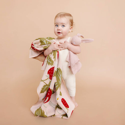 Baby holding The Blueberry Hill - Blanket Strawberry Bunny Organic Baby Decor Spring Summer: Blush with a soft knit bunny toy, cozy neutral background, stylish essentials for little ones and moms.