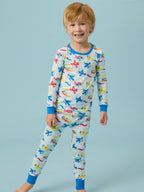 Smiling young boy wearing the RuffleButts + RuggedButts - SoftSnooze™ Kids Bamboo Viscose Plane Parade Long Sleeve Pajama Set featuring colorful airplanes on a light background, styled for comfort and playful bedtime.