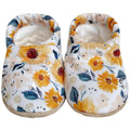 Soft floral baby shoes with yellow and orange blossoms and green leaves on a white background, cozy and breathable, part of CLAMFEET - MOLLIE collection.