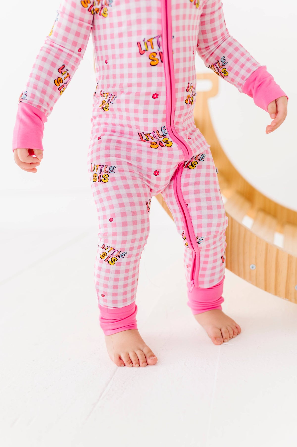 Child wearing a pink and white checkered onesie with cartoon characters on a white background