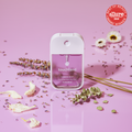 Touchland - Pure Lavender Power Mist Hydrating Hand Sanitizer bottle on pink surface surrounded by dried lavender, eucalyptus, and white flower petals, showcasing an award badge.