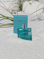 True Ocean - Coastal - a beach perfume bottle and packaging set on white sand with green beach grass, evoking a fresh coastal vibe for stylish kids and moms.