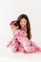 Two children in matching pink and white pajamas with cartoon characters on a white background.
