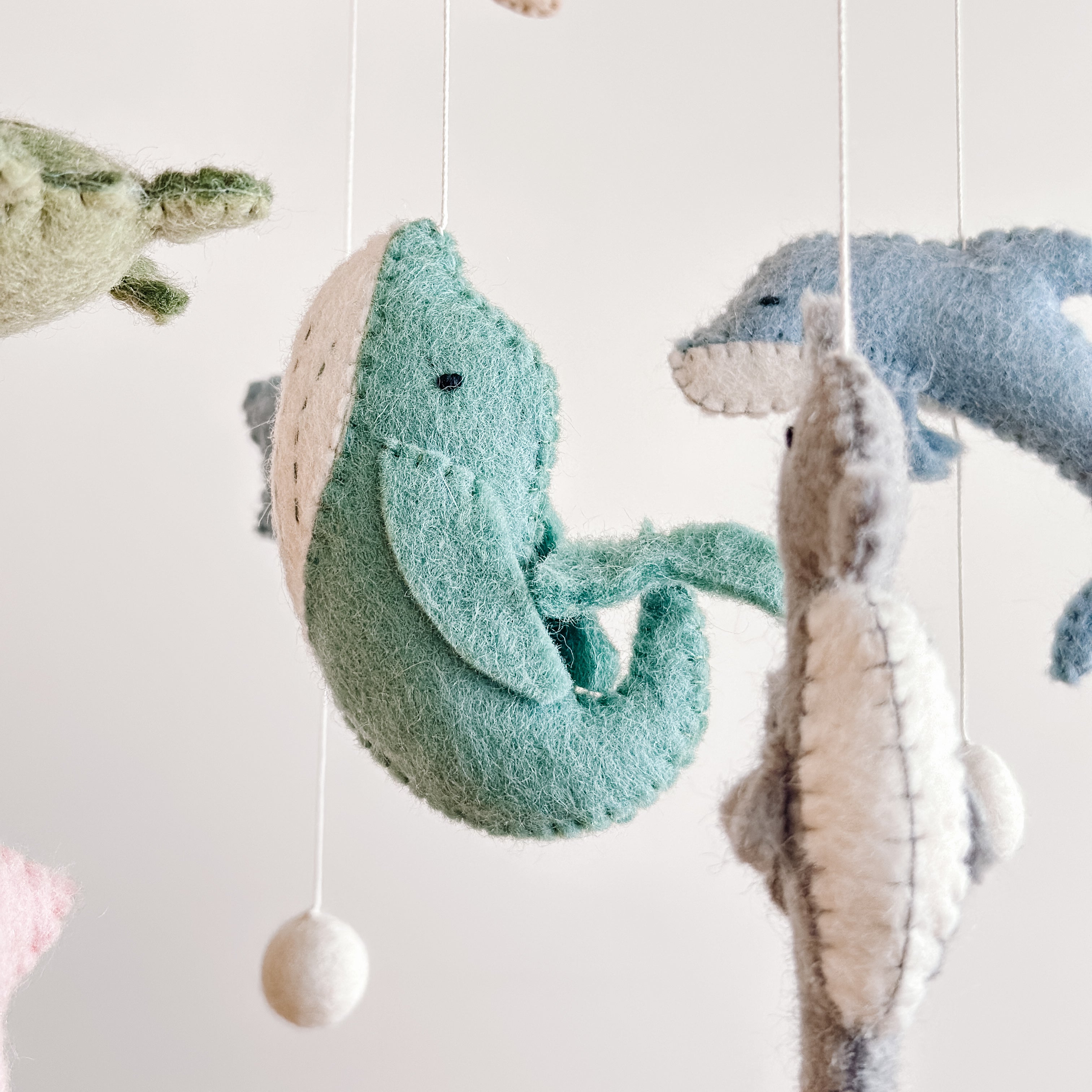 Close-up of handcrafted felt sea life animals including a whale, dolphin, and turtle hanging from strings in the Mobile - Felt Baby - Sea Life, perfect for a cozy baby nursery.