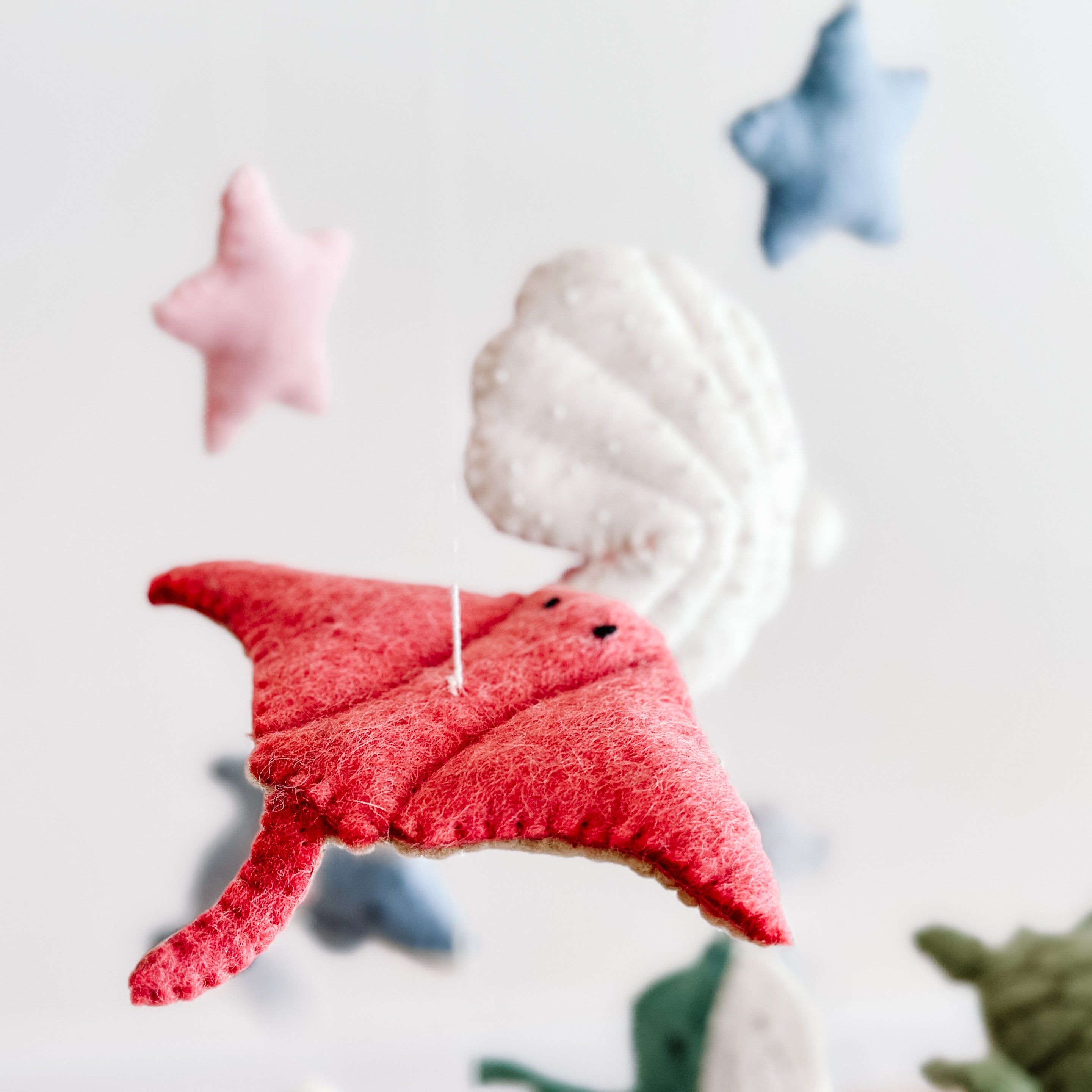 Soft felt sea life shapes including a red manta ray, white seashell, and pastel stars hanging from a Mobile - Felt Baby - Sea Life, perfect for a cozy baby nursery.