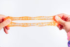 A pair of hands stretching a translucent orange and white glittery slime against a plain white background.