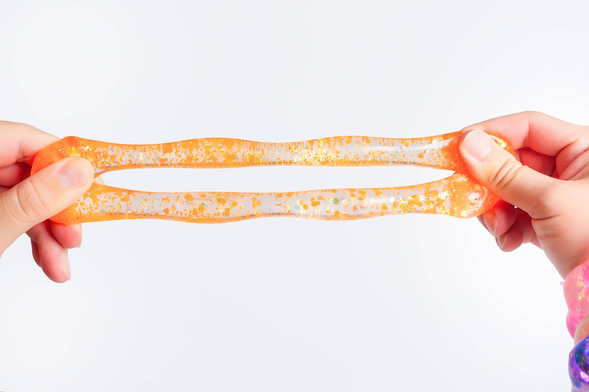 A pair of hands stretching a translucent orange and white glittery slime against a plain white background.