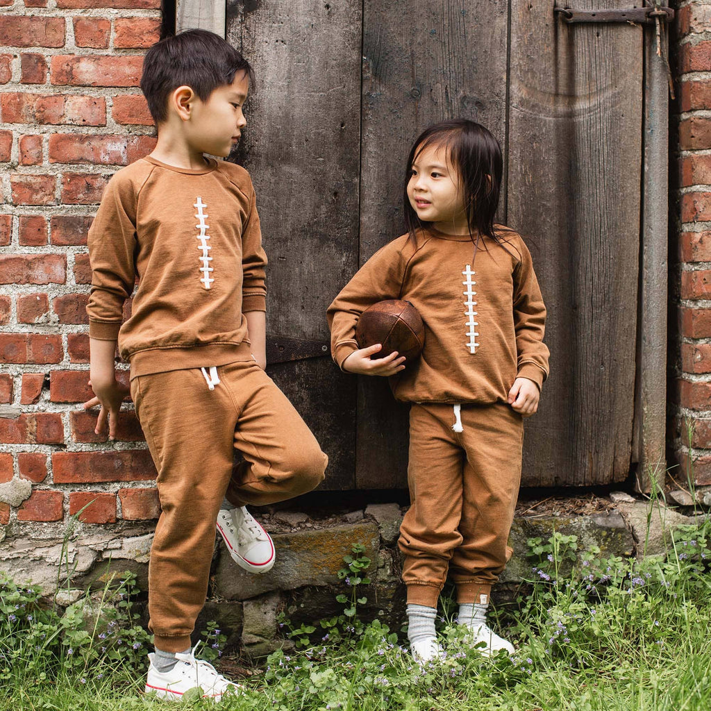 Two children in matching brown football outfits standing against a brick wall.