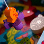 Colorful wooden fish shapes suspended by string in a close-up of the "My Very First Games - Here, Fishy, Fishy! Magnetic Game" designed for imaginative play and early learning.