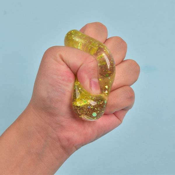 A hand squeezing a translucent yellow glittery stress toy against a light blue background.