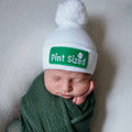 Newborn baby peacefully sleeping wearing the ilybean - Pint Sized Irish Baby Newborn Hospital Hat - Gender Neutral in white with green embroidered patch, wrapped in a soft green blanket.