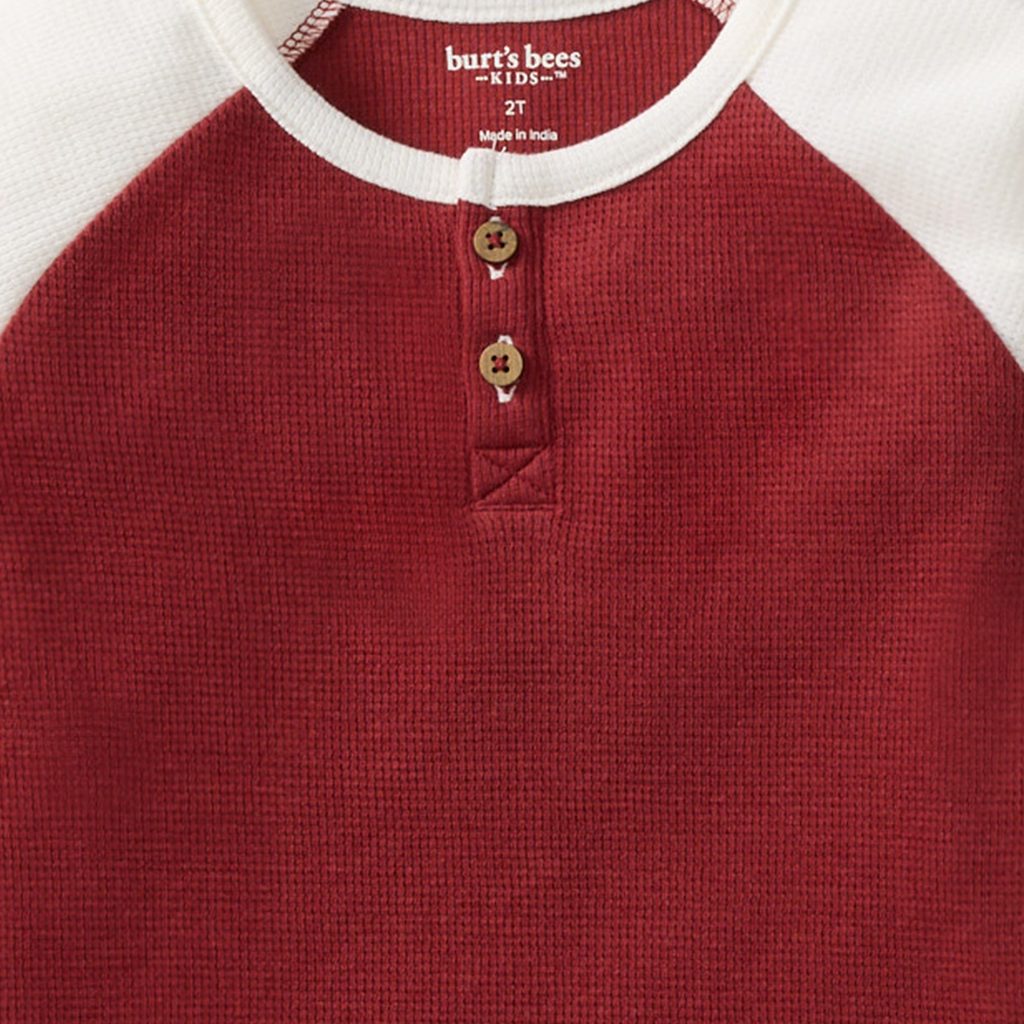 Close-up of the textured brick red thermal fabric of the Burt's Bees Baby - Thermal Organic Boy Tee & Pants Set - Brick Red featuring wooden buttons and white crew neckline, perfect for cozy baby essentials and stylish kids clothing.