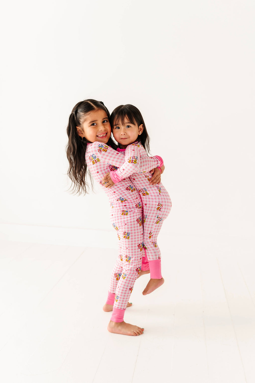 Two children wearing pink pajamas with cartoon characters on a white background