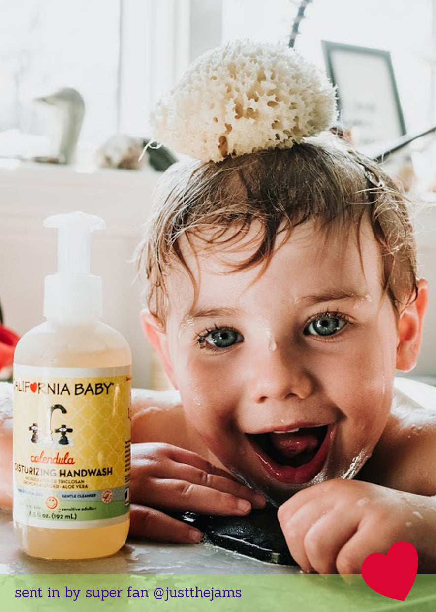 Happy toddler in bath with a natural sponge on their head next to a bottle of California Baby - Calendula™ Moisturizing Handwash, capturing cozy baby essentials and playful moments.
