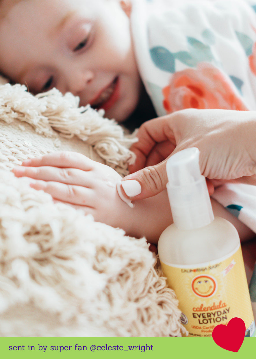 Close-up of a child’s hand receiving a gentle application of California Baby - Calendula™ Everyday Lotion from a caregiver, surrounded by soft, cozy textures, reflecting a nurturing moment consistent with a curated children’s boutique ethos.