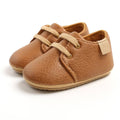 Pair of Urban Tots - Taylor Leather Kicks - Brown baby shoes made from soft leather with beige laces, designed for comfort and style in a curated children’s boutique.