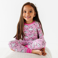 Smiling young girl wearing Kiki + Lulu - Pink Zzz Kids Pajamas with playful moon, cloud, and star patterns in soft pink, showcasing cozy, stylish kids clothing from a curated children’s boutique.