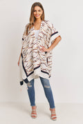 Woman wearing the Love and Repeat - TASSEL LINE PRINTED OPEN FRONT KIMONO: MULTI over a white top and distressed blue jeans, styled with white strappy heels, showcasing a flowing and patterned multi-color kimono perfect for stylish kids clothing boutiques.