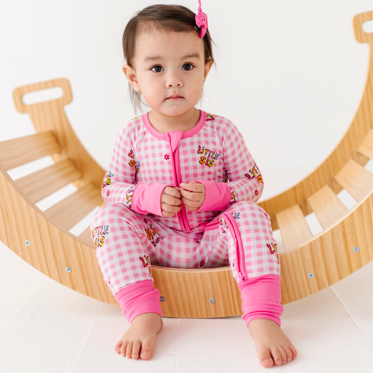 Child wearing a pink checkered outfit with cartoon characters, sitting on a wooden toy.