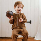 Child wearing a brown outfit with a football design, holding a vintage-style football.