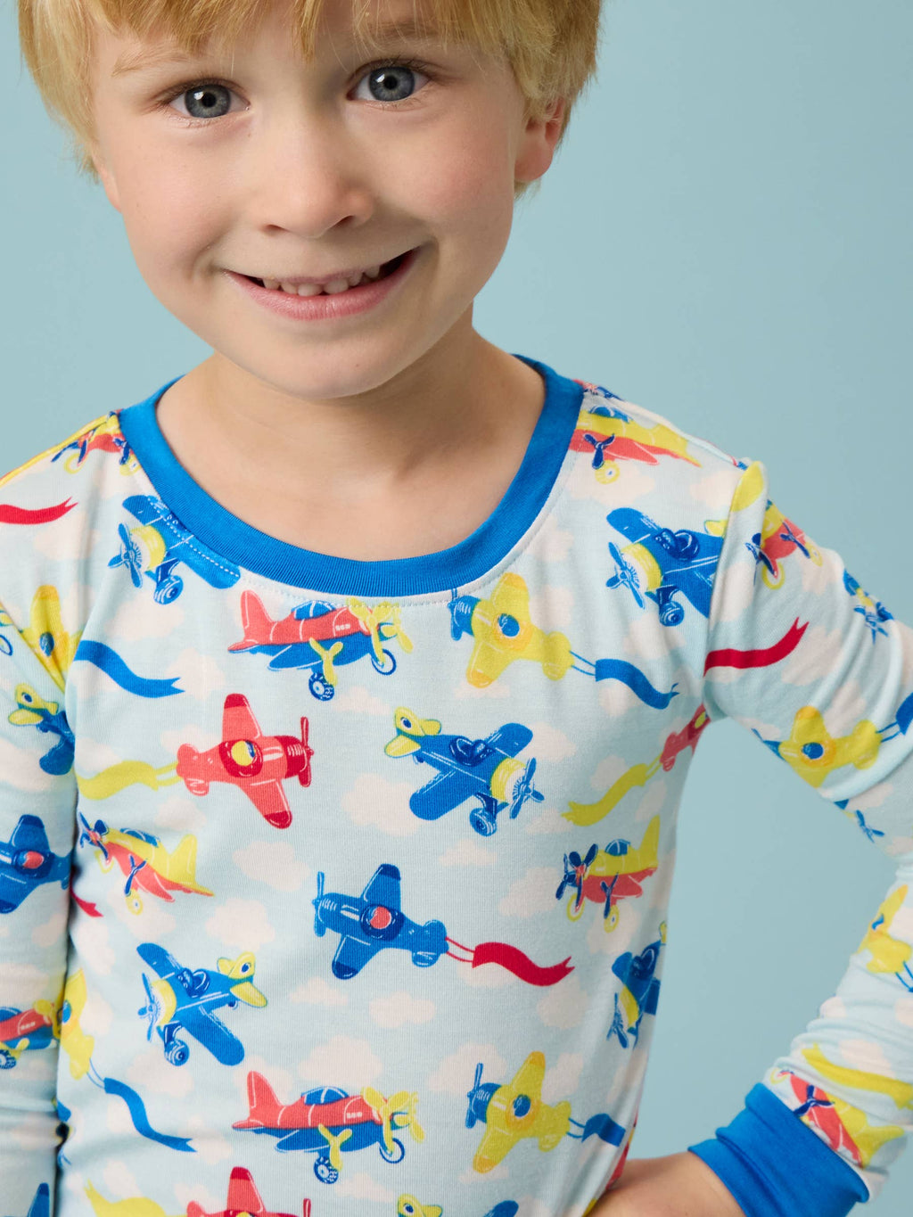 Young child wearing RuffleButts + RuggedButts - SoftSnooze™ Kids Bamboo Viscose Plane Parade Long Sleeve Pajama Set with colorful airplane pattern and blue trim, cozy and stylish for kids.