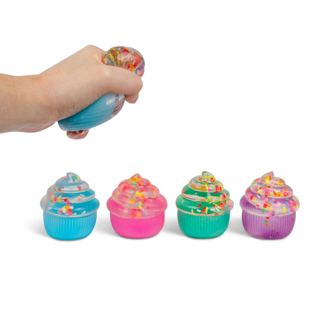 Hand squeezing a colorful squishy toy shaped like a cupcake with sprinkles with four additional cupcake squishies lined up on a white background.