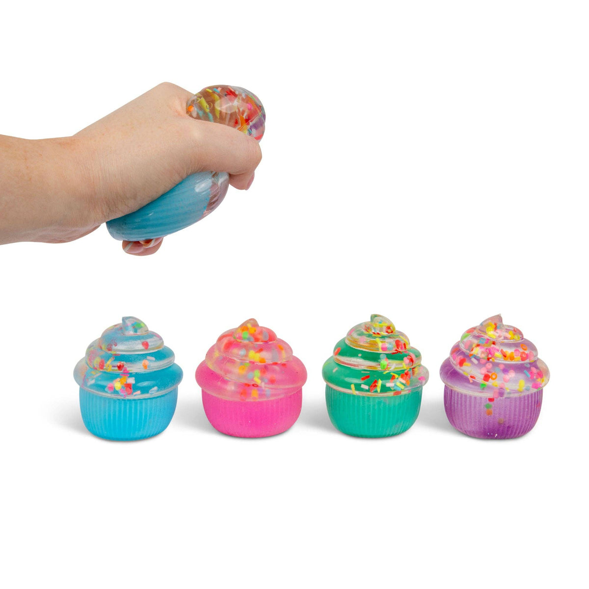 Hand squeezing a colorful squishy toy shaped like a cupcake with sprinkles with four additional cupcake squishies lined up on a white background.