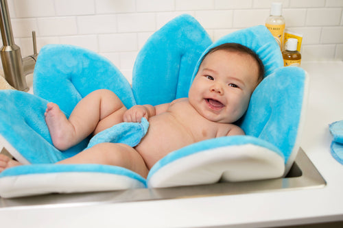 Happy baby comfortably resting in a soft blue petal-shaped bath cushion designed for safe and cozy bath time care, featuring Blooming Baby - Blooming Bath Original: Blue.