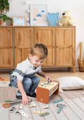 A young child playing on the floor with the Speedy Monkey - Toolbox - Workbench, surrounded by colorful wooden tools and parts in a cozy, stylish children’s room setting.