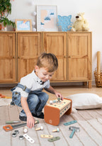 A young child playing on the floor with the Speedy Monkey - Toolbox - Workbench, surrounded by colorful wooden tools and parts in a cozy, stylish children’s room setting.